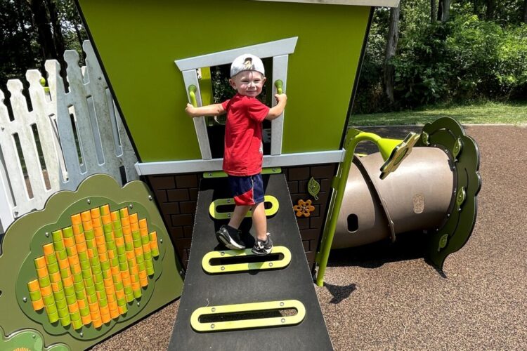 young boy climbing up ramp into green playground structure