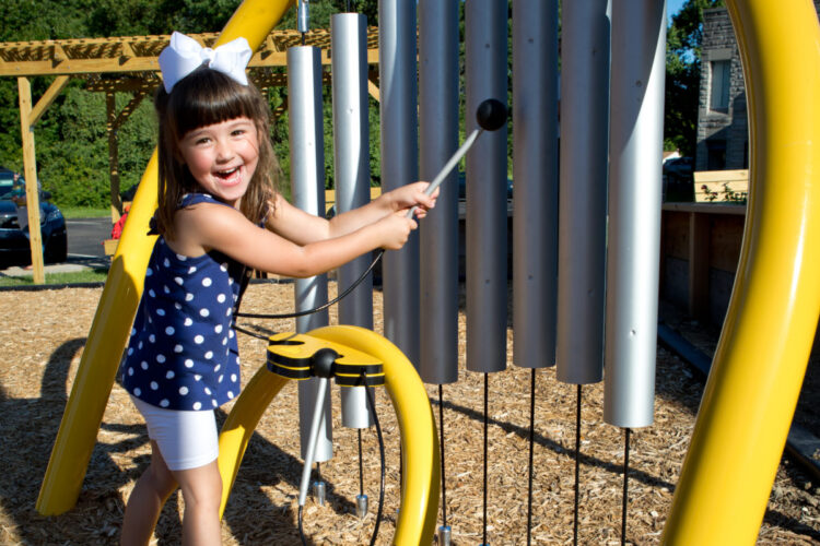 young girl playing with toy bells built into playground set