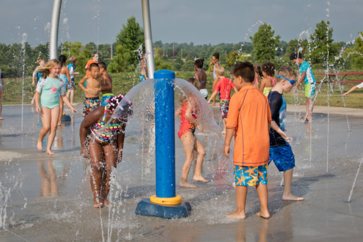 kids playing with water spraying from ground and from poles around splash pad