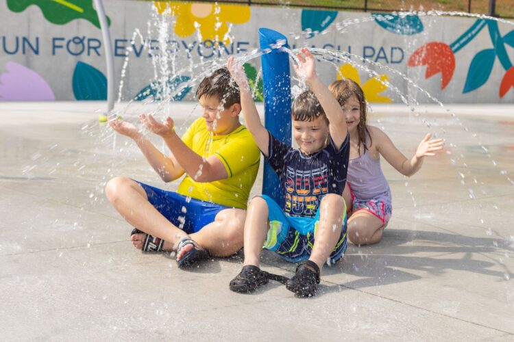 three little kids laughing as they are getting sprayed by water post