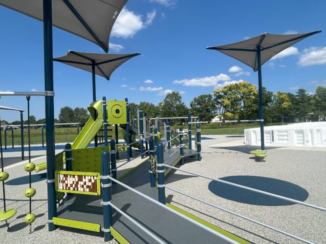 Green, blue, and gray play structure with wheelchair accessibility, and 3 shade sails