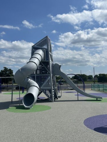 Multi-level play structure with one curly tunnel slide and a double slide on rubber surfacing.