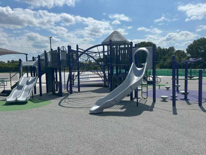 play structure on rubber surfacing with curvy slide, two side by side bumpy slides, climbing net, and pod walkers