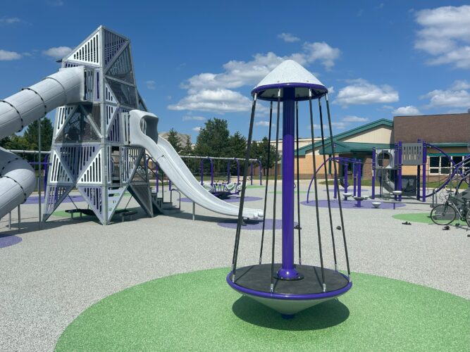 Multi-person spinner on safety surfacing and multi-level play structure with 2 slides