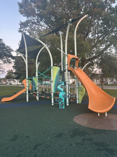 play structure with integrated shade, orange slides, and multiple climbing options