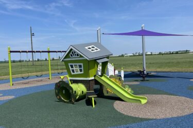 imaginary play house with a slide and a tunnel, 2 bays of swings, and purple fabric shade