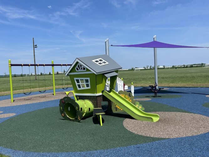 imaginary play house with a slide and a tunnel, 2 bays of swings, and purple fabric shade