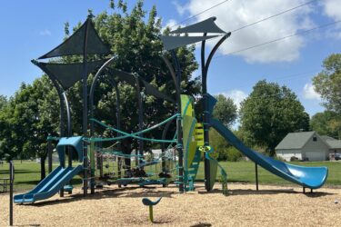 Blue and green play structures for 5-12 year old kids with 3 slides, climbing ropes, and integrated fabric shade