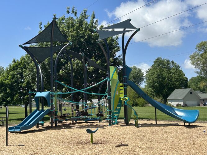 Blue and green play structures for 5-12 year old kids with 3 slides, climbing ropes, and integrated fabric shade