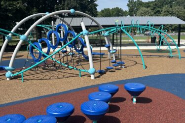 7 round steppers on red, blue, and brown safety surfacing, with a climbing play structure