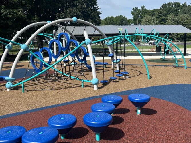7 round steppers on red, blue, and brown safety surfacing, with a climbing play structure