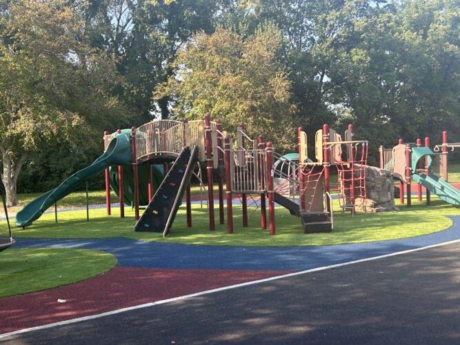red, brown and green play structure with slides, a climbing wall, and climbing nets for kids ages 5-12