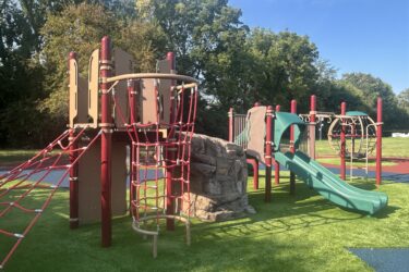 red, brown, and green play structure with climbing nets, climbing rock, and slide