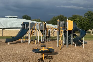 orange, blue, and sliver play structure with slides, climbing nets, and multi-person spinner