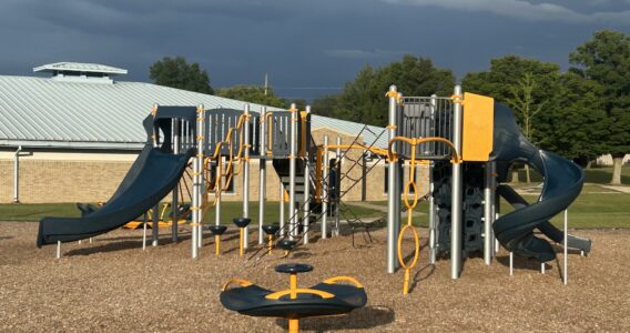 orange, blue, and sliver play structure with slides, climbing nets, and multi-person spinner