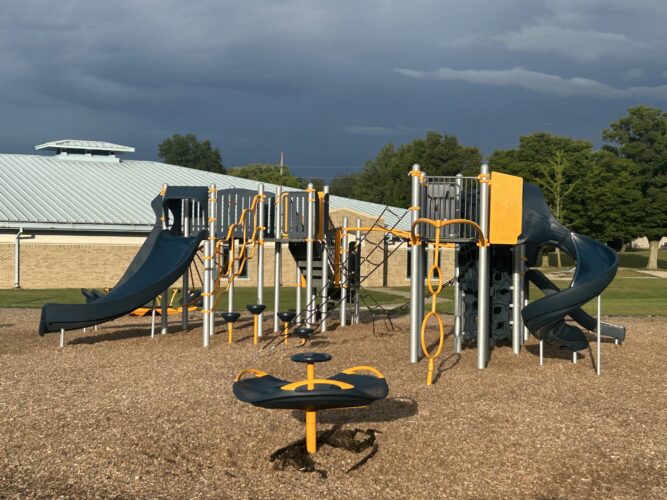 orange, blue, and sliver play structure with slides, climbing nets, and multi-person spinner