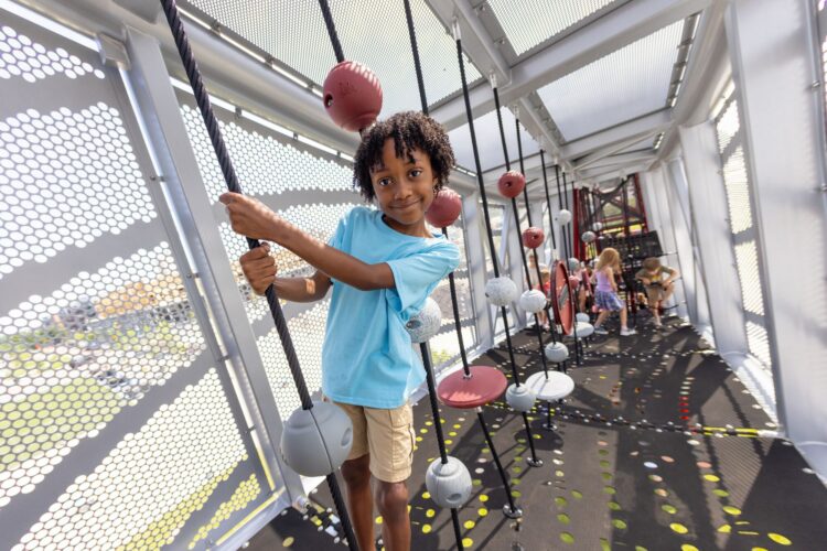 little boy playing on a rope inside a connecting bridge to 2 large towers