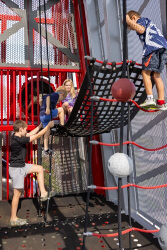 kids playing on climbing ropes and belts inside an enclosed bridge